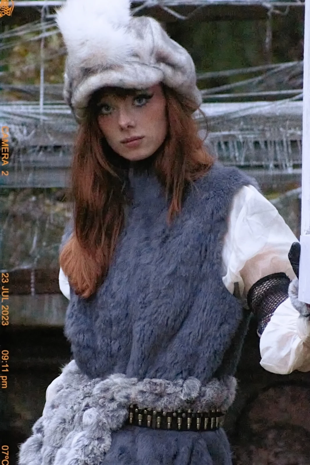 Close-up portrait of a red-haired model in gray furry outerwear and an animal-shaped headpiece.