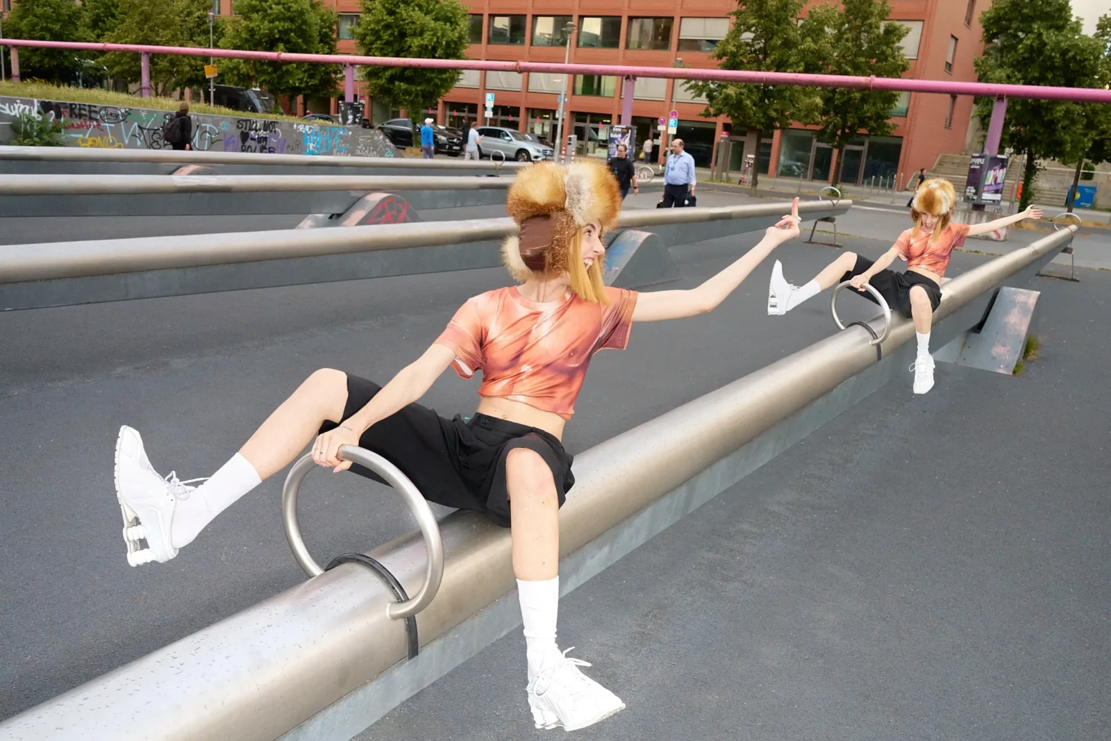 Model wearing a pink top, black shorts and white boots leaning dramatically against a metal railing in Berlin.