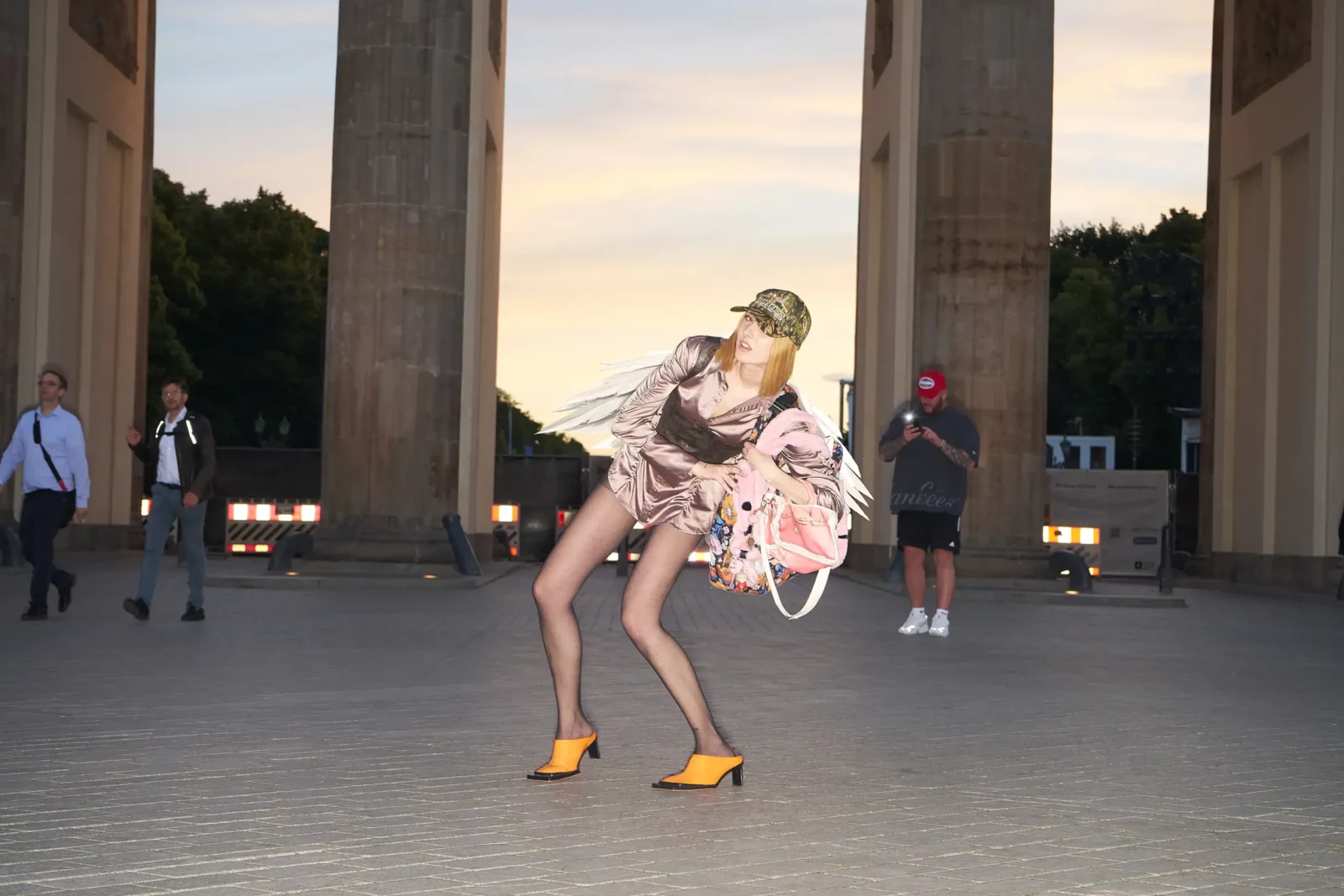 Fashion portrait of a model in a sculptural pink-and-black outfit and yellow heels beneath the Brandenburg Gate.