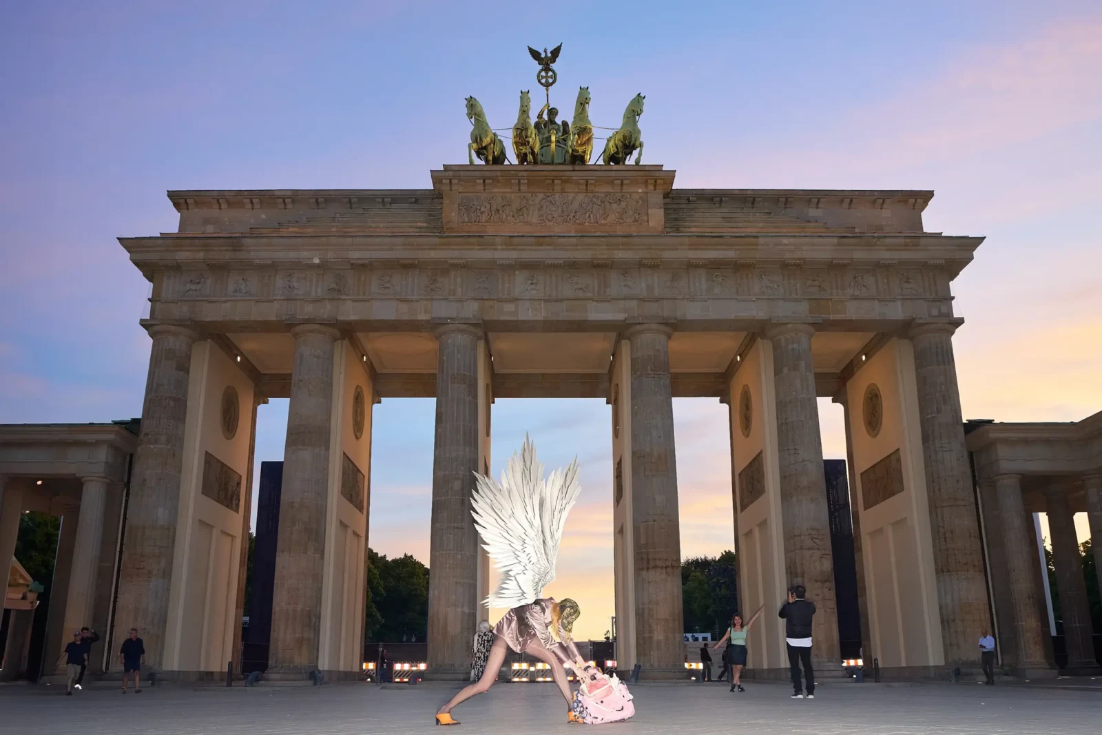 Wide view of a fashion model with a large white feather headpiece posing below the Brandenburg Gate.