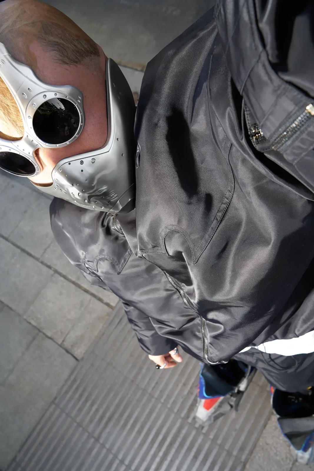 Overhead close-up of a gray-clad figure wearing oversized white sunglasses on a tiled pavement.