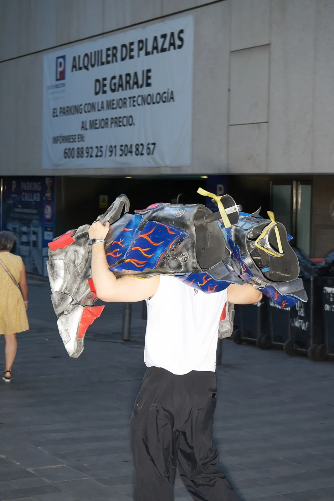 Person carrying a colorful bundle of fabric overhead on a city sidewalk outside a building.