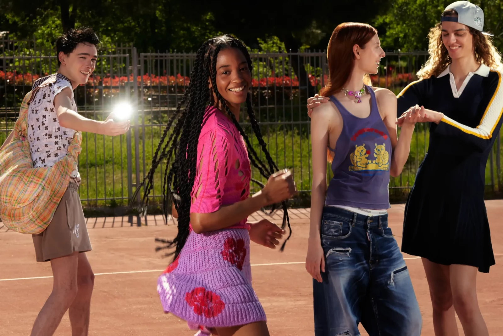 Group of models in colorful outfits chatting near a fence in evening light.