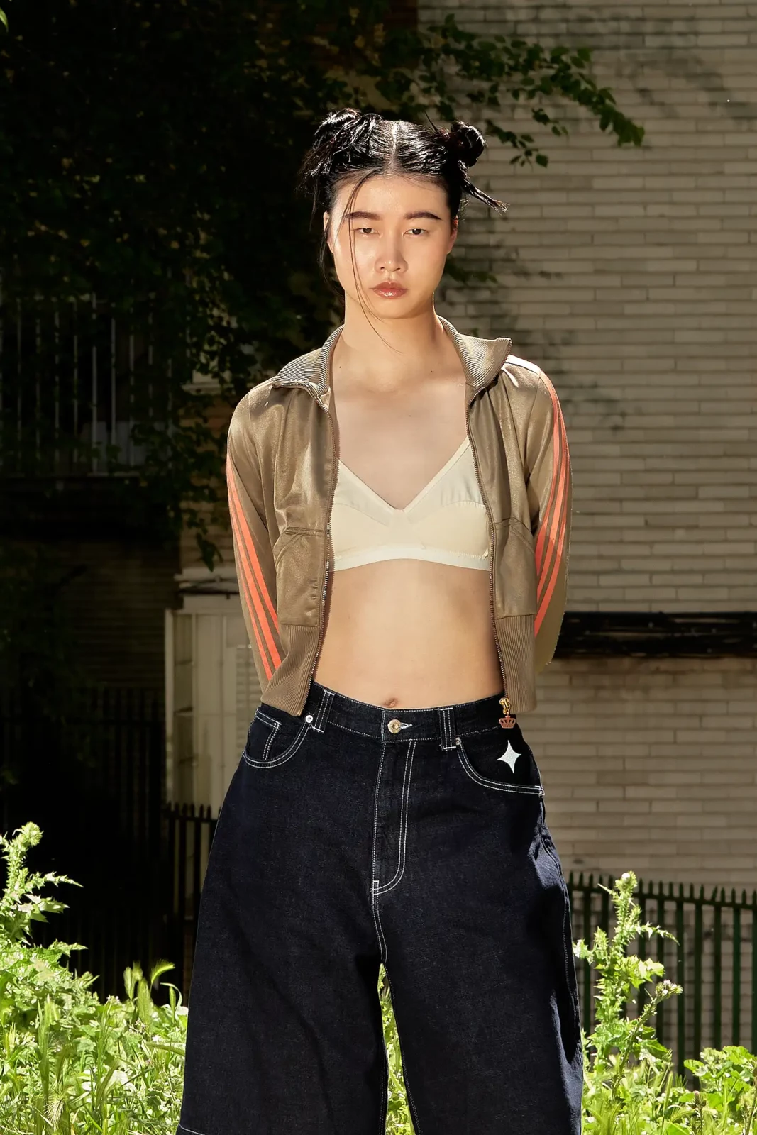Fashion model wearing a cropped top and oversized black trousers in front of a brick building.