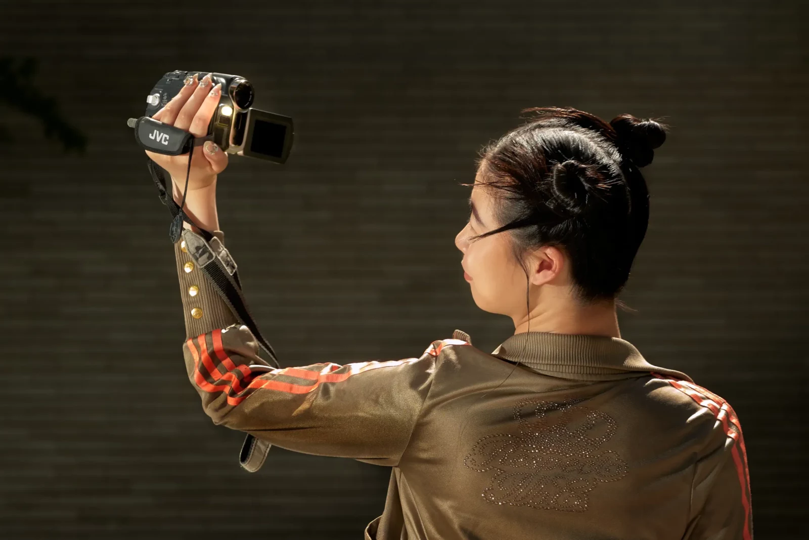 Side-profile model holding a handheld camcorder in warm evening light.