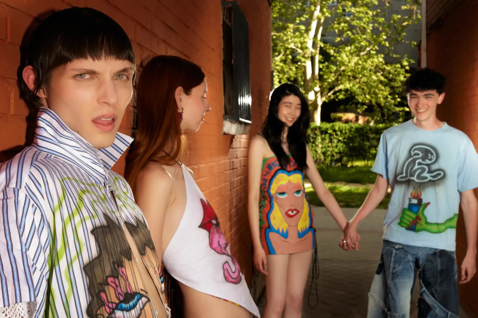 Four models standing together on a sunlit urban pathway in colorful layered outfits.