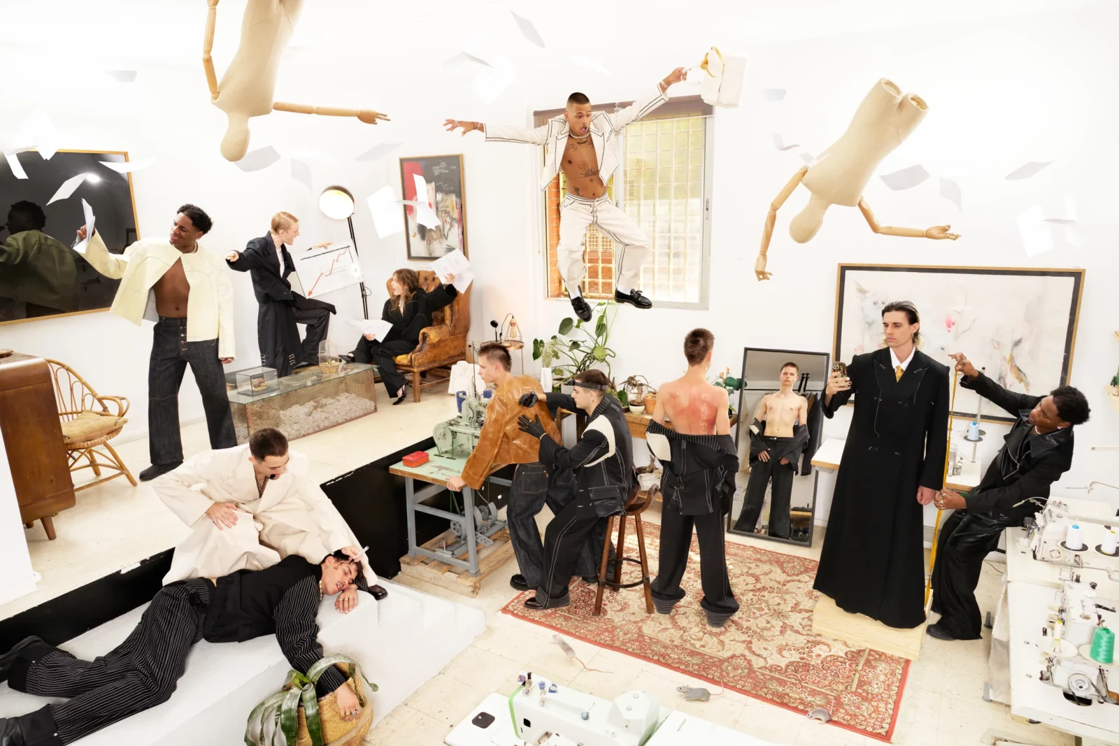Wide editorial photograph of a crowded art-filled room with performers and guests gathered among framed pictures and suspended figures.