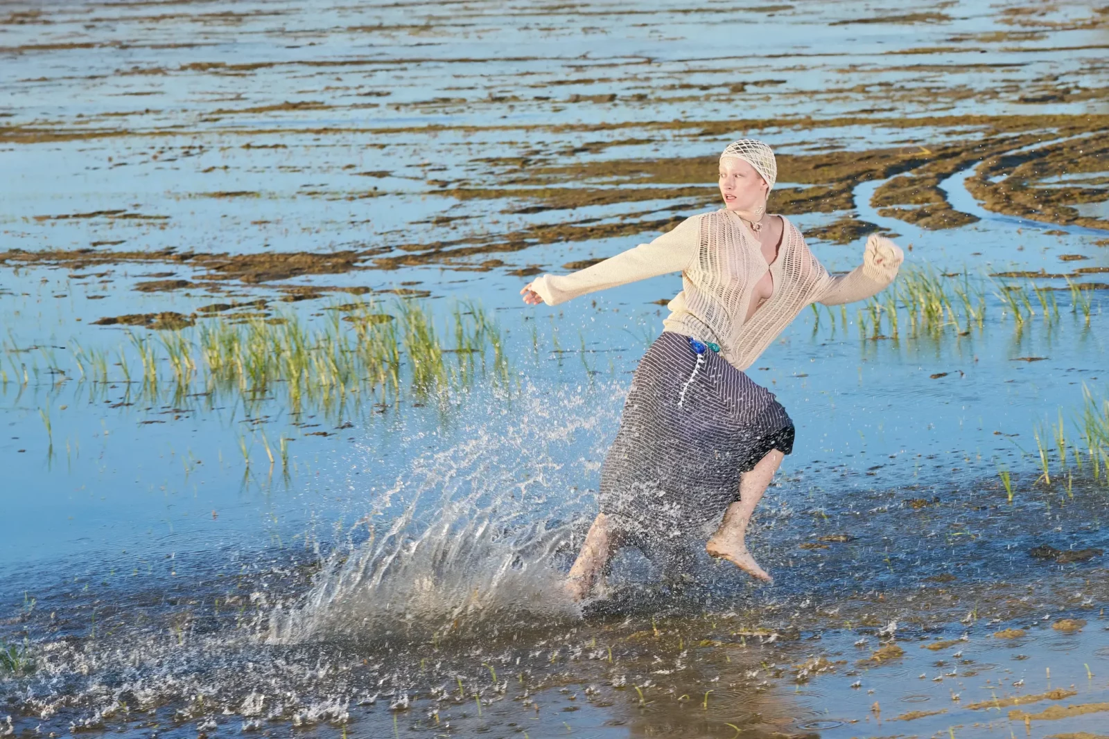Model splashing through shallow water with outstretched arms in an outdoor editorial.