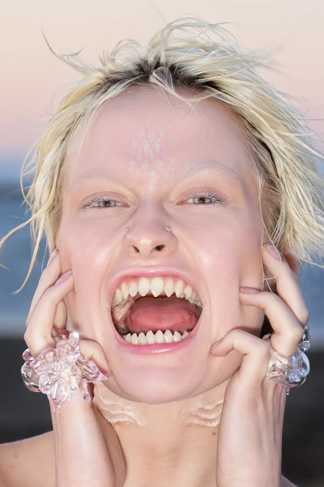Close-up portrait of a short-haired blonde fashion model with an open mouth and statement earrings.