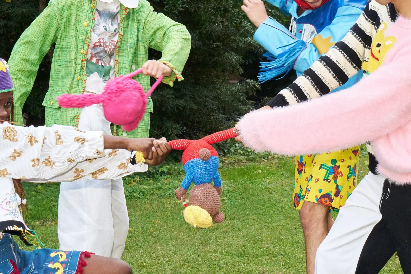Close-up of colorful layered streetwear and playful accessories as two models reach their hands toward each other.