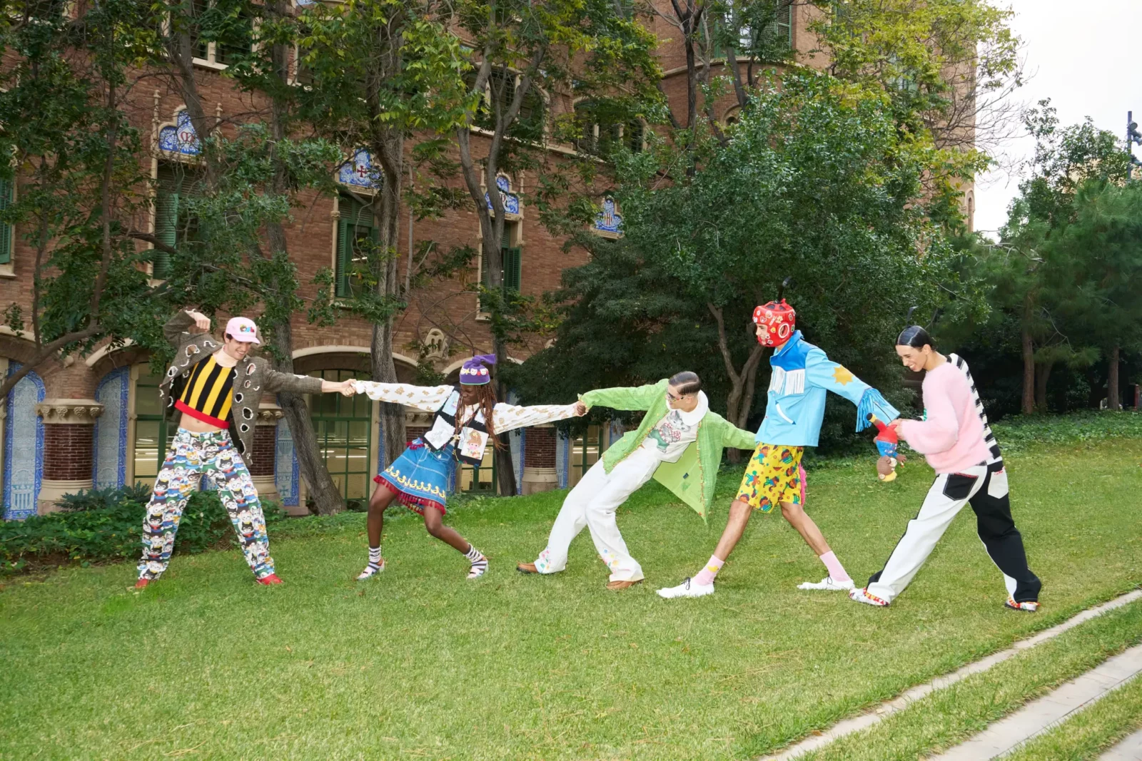 Wide view of models wearing bold patterned streetwear while stretching their arms across a green lawn.