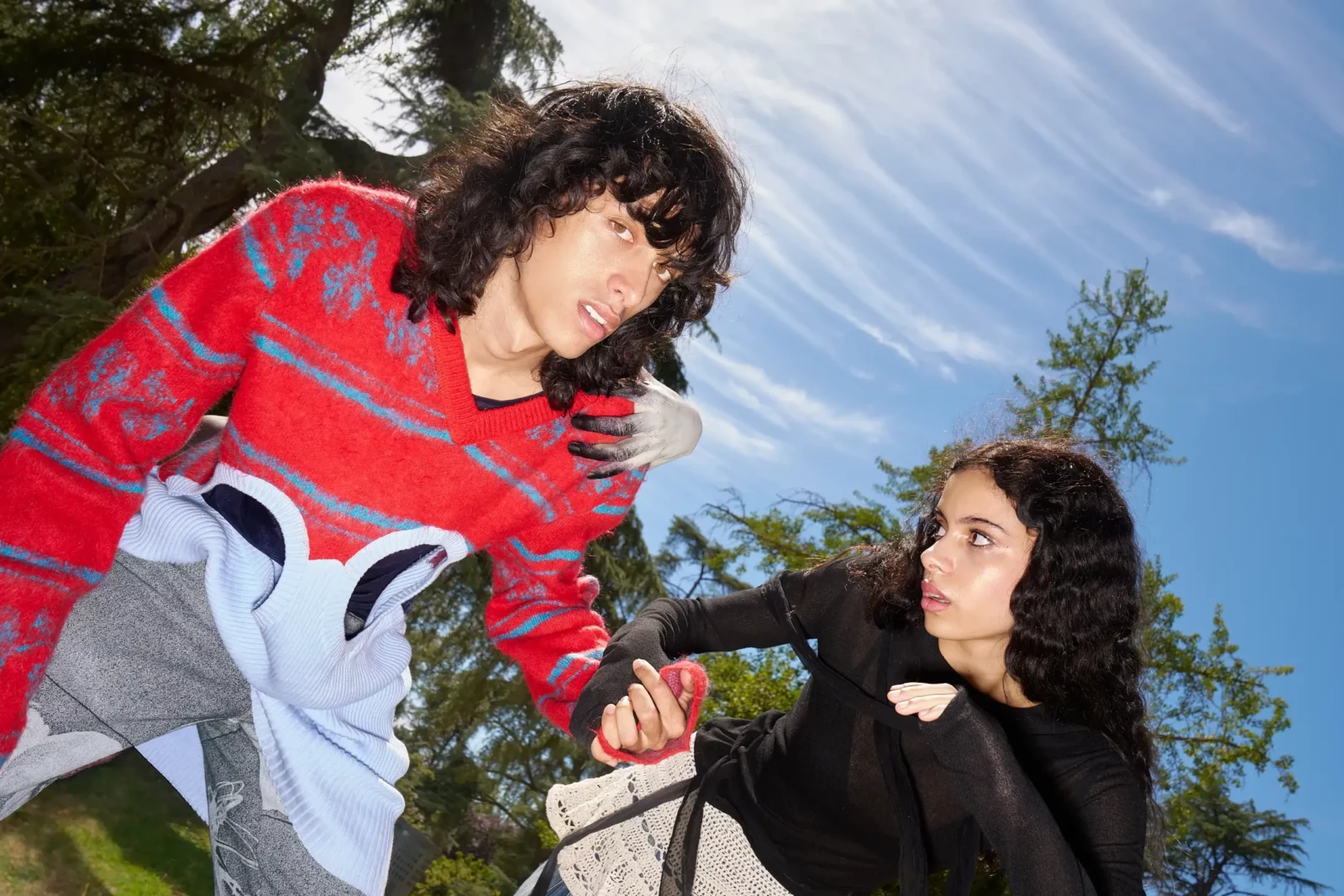 Two models in red and black graphic streetwear interacting beneath a blue sky.