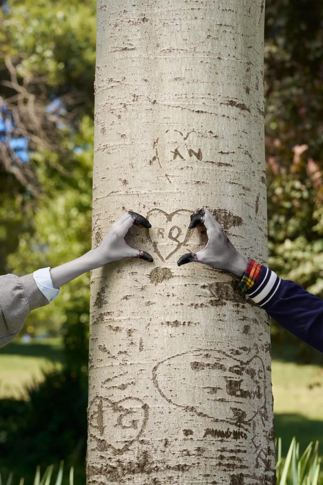 Silver-gloved hands reaching around a tree trunk in a surreal outdoor fashion scene.