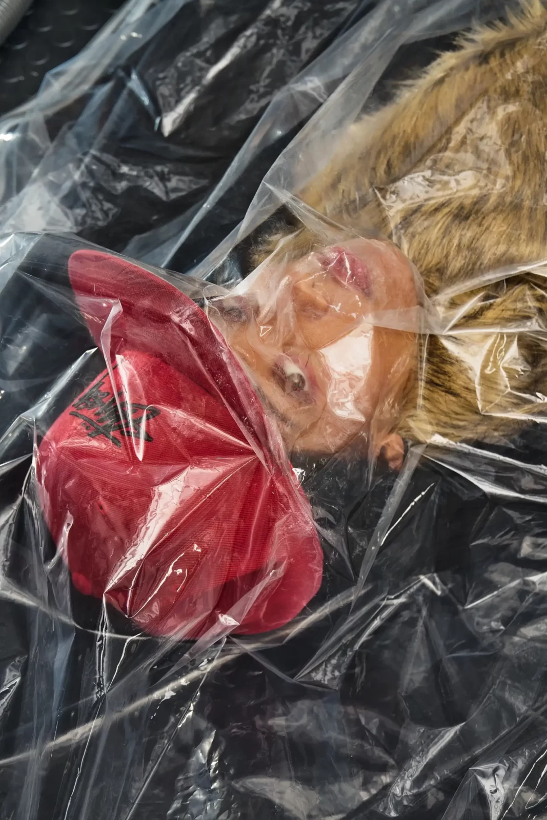 Close-up of a model in red headwear photographed through folded clear plastic.