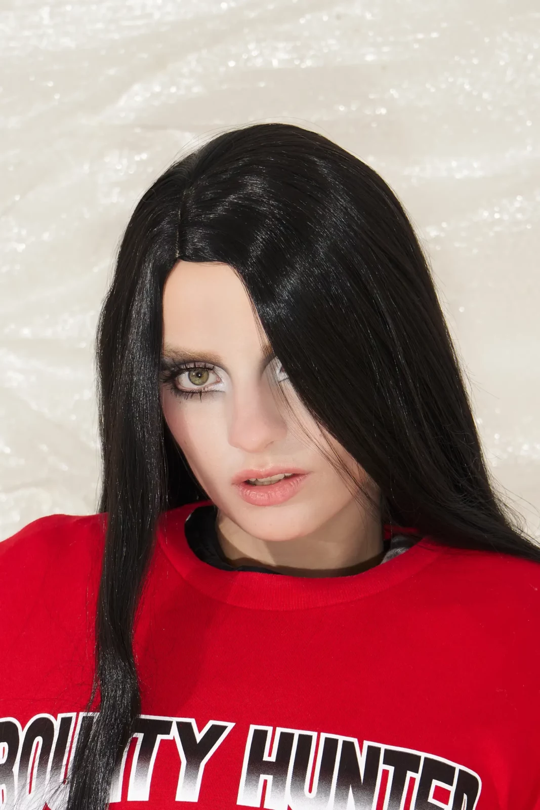 Beauty portrait of a dark-haired model wearing a red graphic T-shirt against a pale textured backdrop.