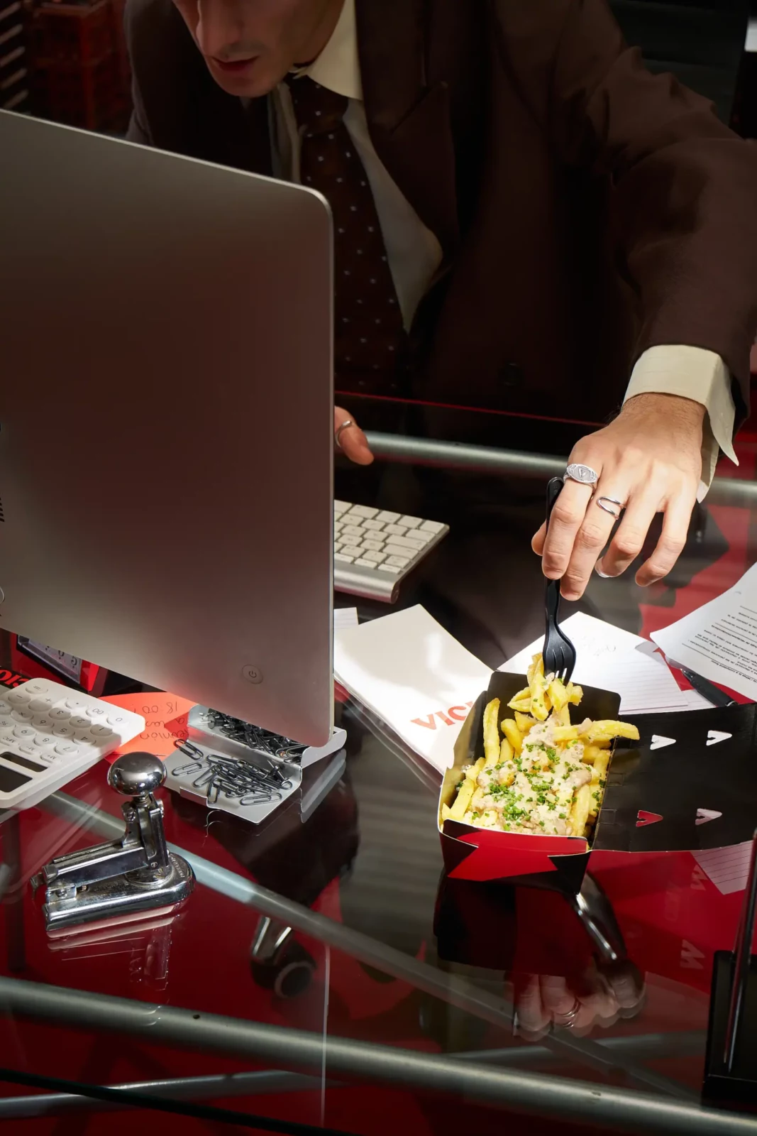 Close-up of a person using a laptop beside a red takeaway food box containing fries.