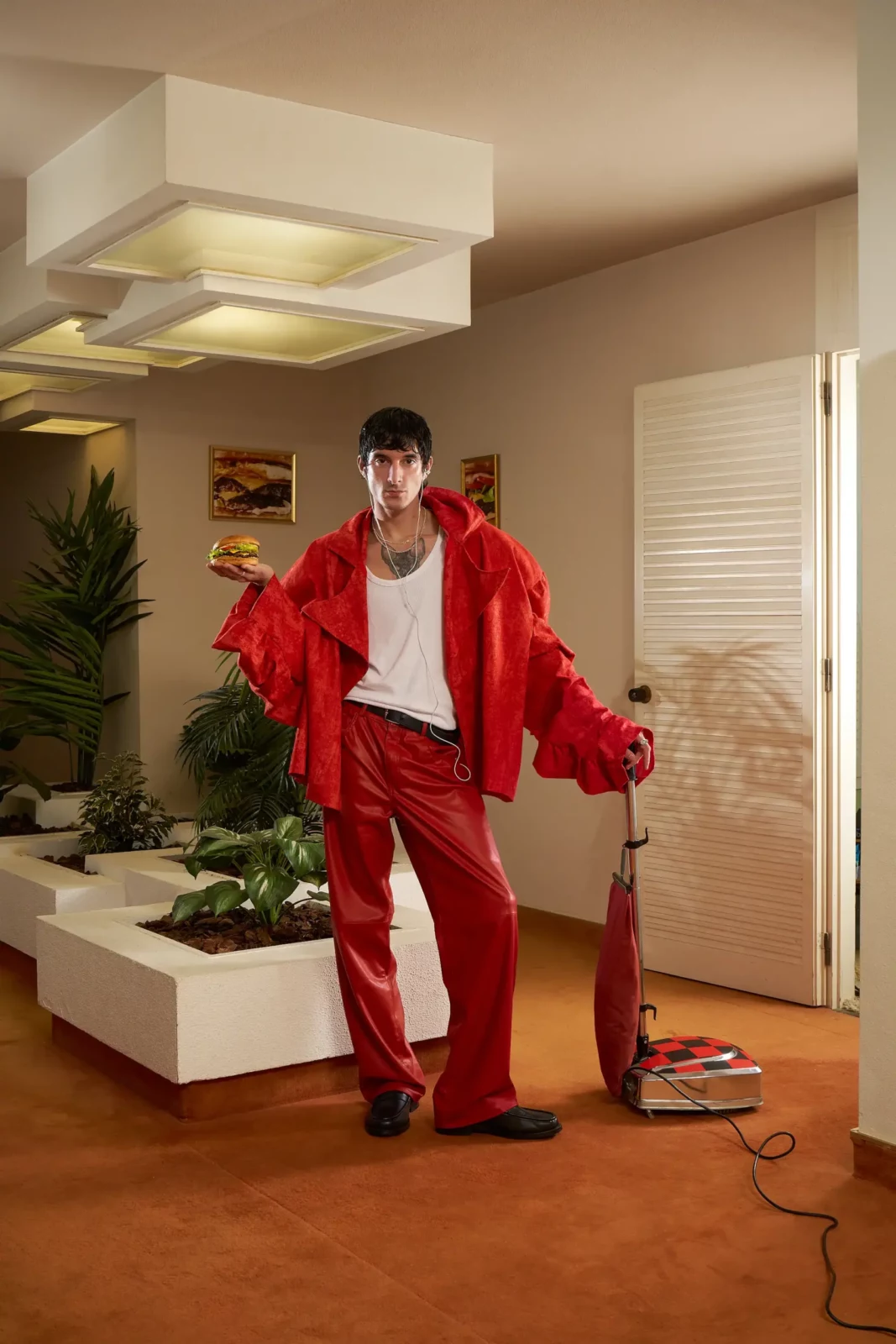 Fashion model wearing a bright red tracksuit and holding a food bag in a warmly lit living room.