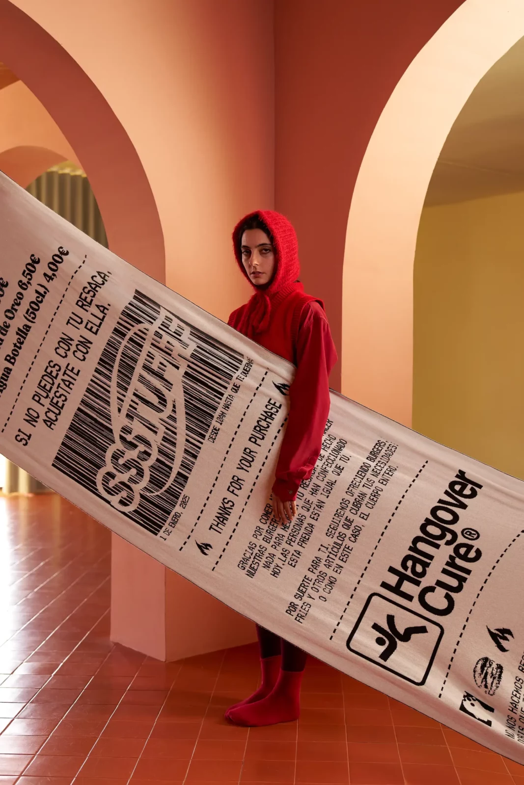 Two models in red and white clothing posing behind large printed newspapers in a warm-toned hallway.