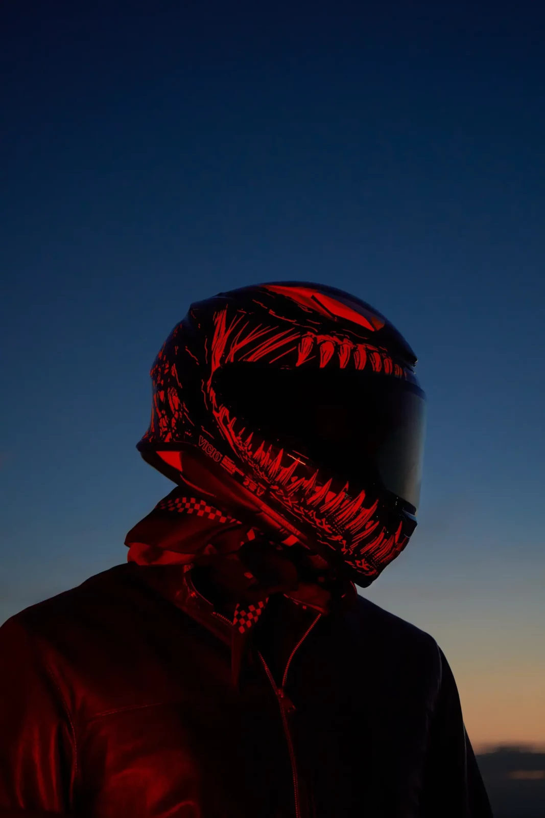 Profile of a motorcyclist in a black helmet with a bold red graphic design against twilight.