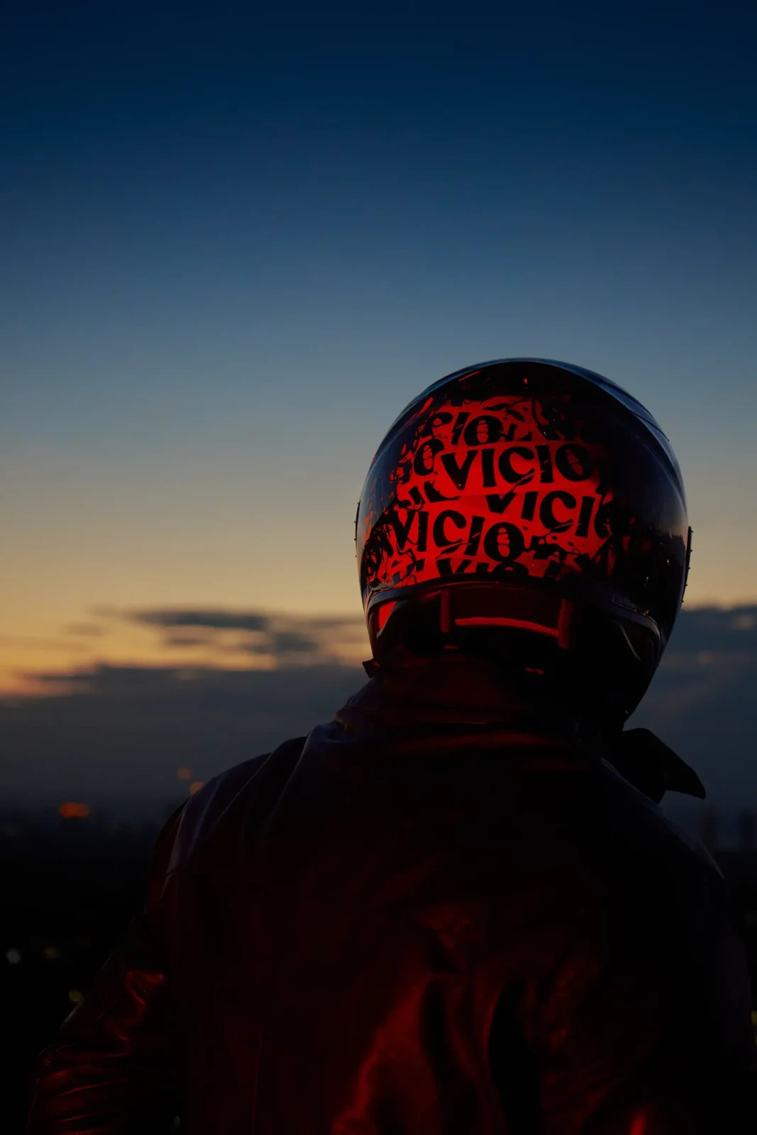 Rear view of a helmeted rider in black clothing facing a deep blue twilight horizon.