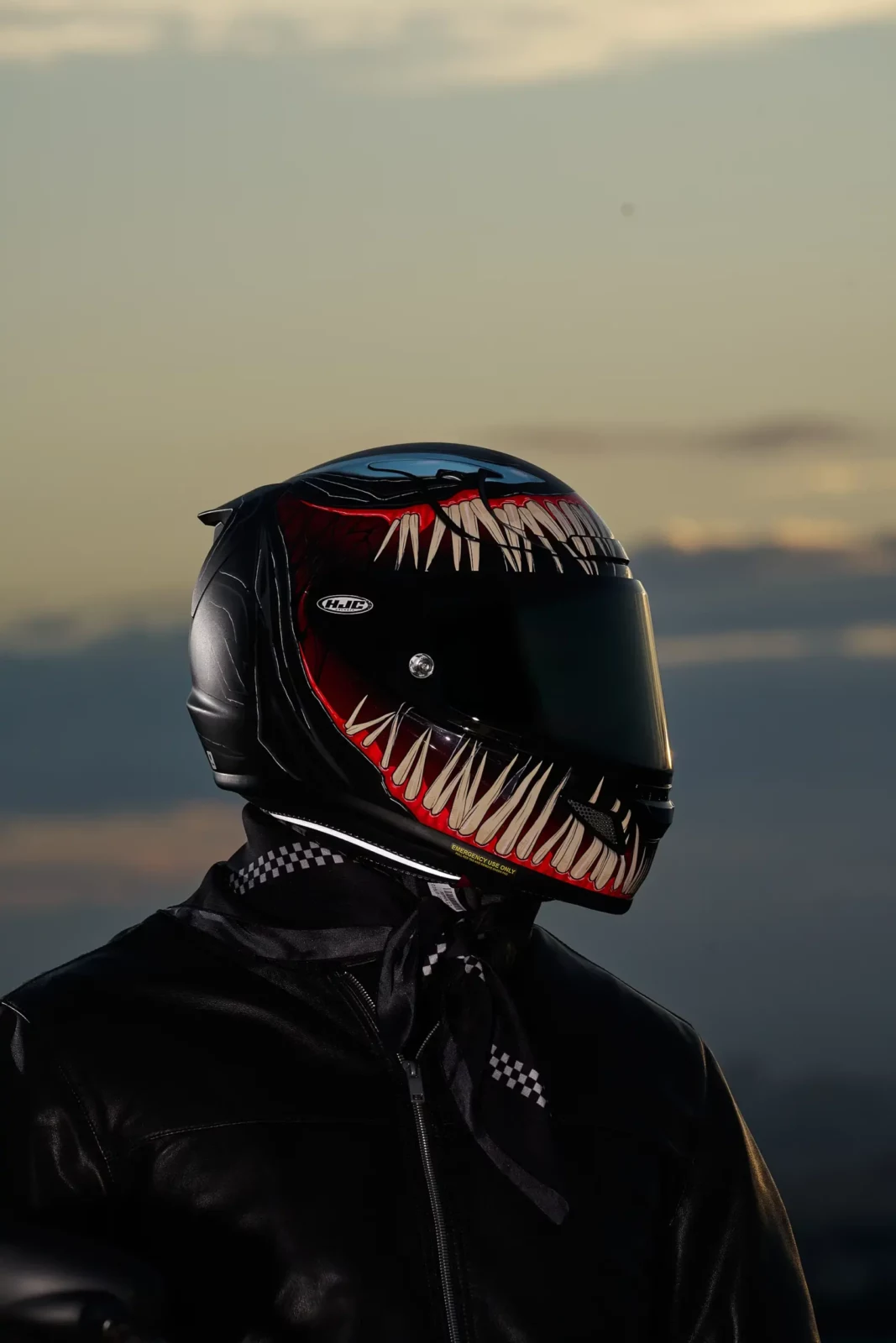 Close-up of a black motorcycle helmet with red graphic lettering against a golden dusk sky.