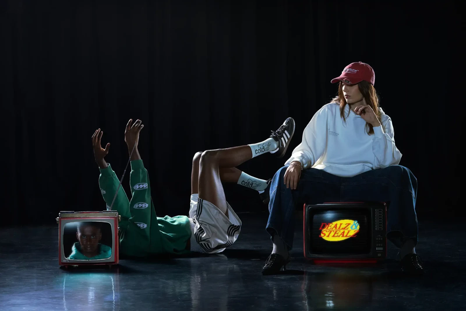 Models in streetwear posing with illuminated vintage television sets against a black studio backdrop.