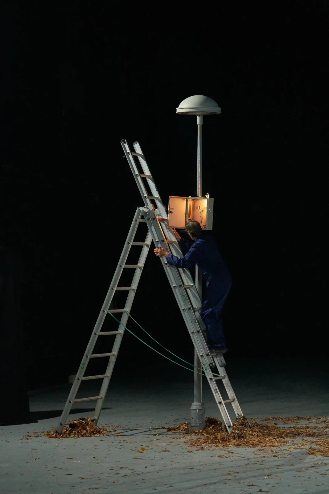 Lone figure standing on a ladder beneath a streetlamp against a dark night sky.