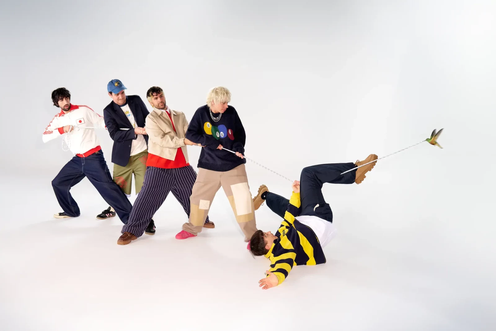 Cupido band members pulling a rope in a playful staged group photograph against a white studio backdrop.
