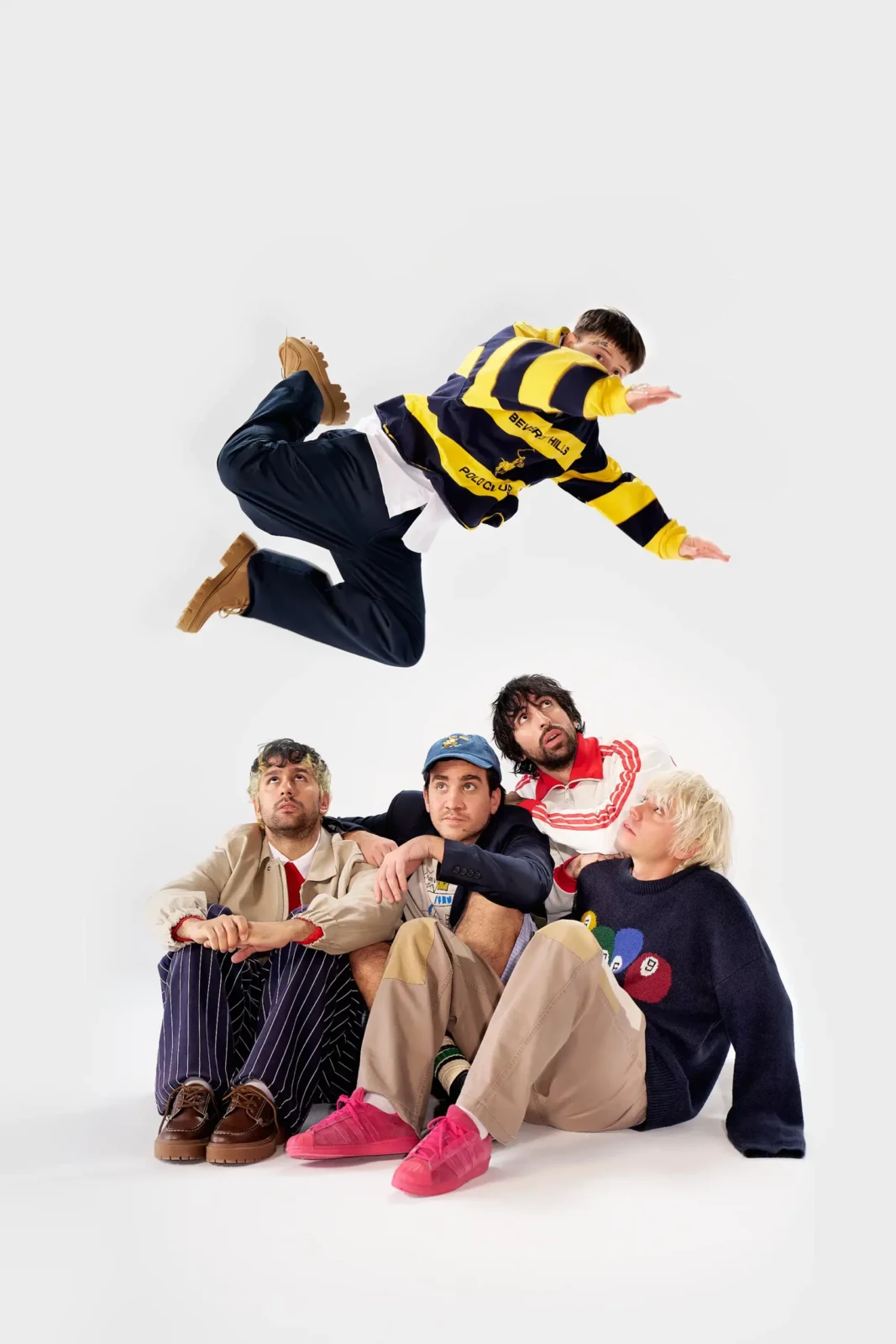 Cupido band members posing in a playful tableau with one member leaping against a white studio background.