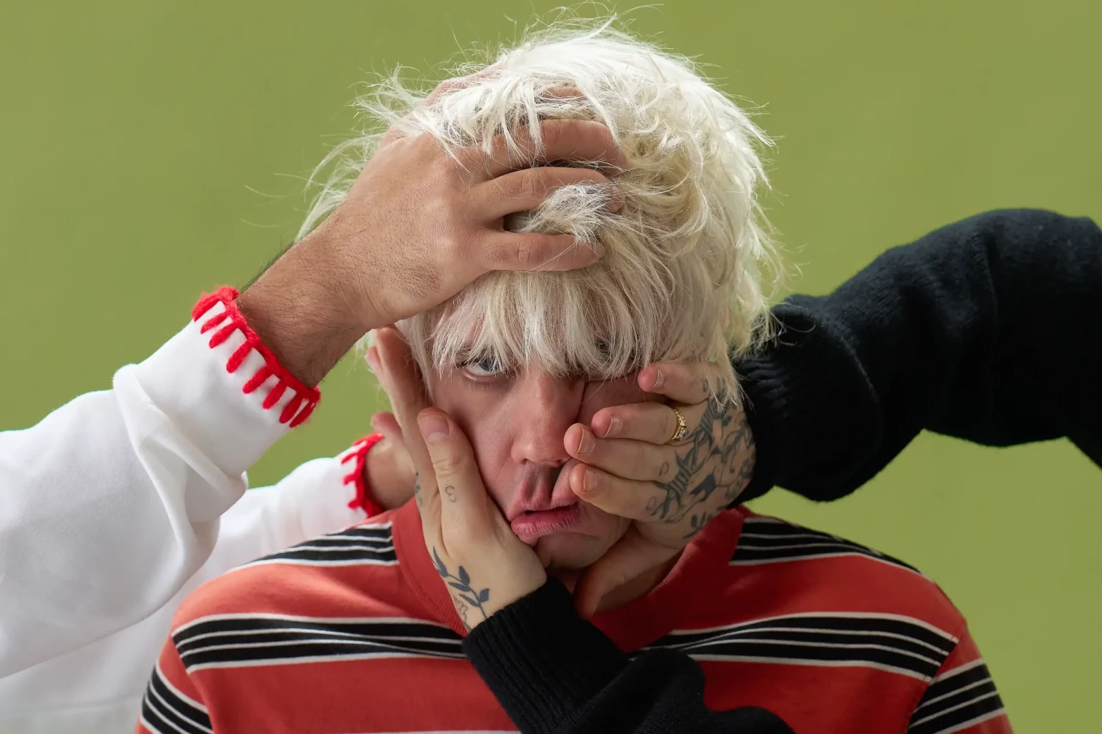 Blond Cupido band member with hands covering his face against an olive green backdrop.