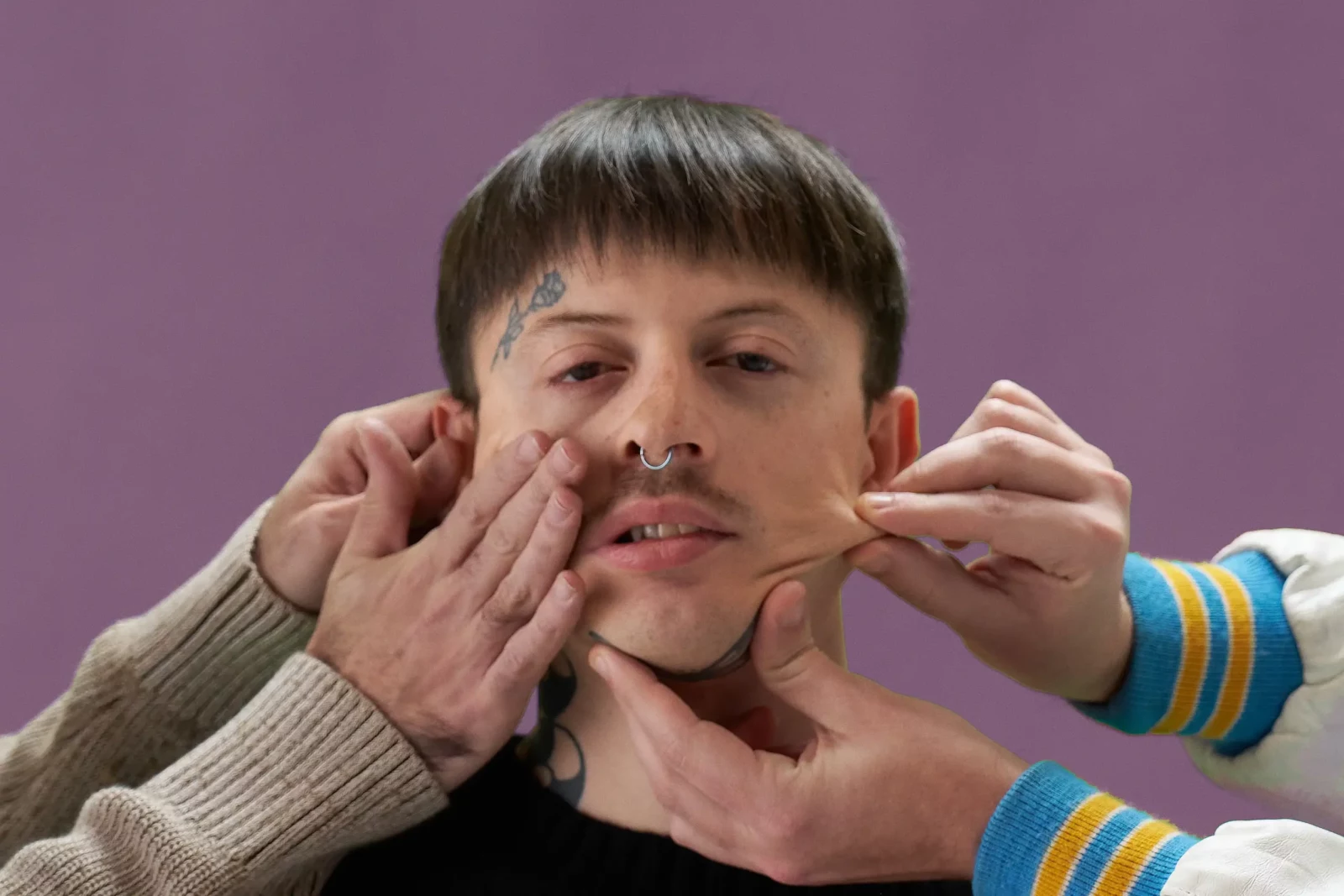 Close-up portrait of a Cupido band member as hands press and stretch his face against a purple backdrop.