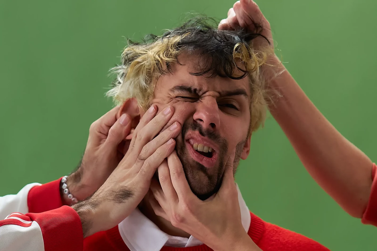 Close-up of a Cupido band member making a strained expression as hands pull his face.
