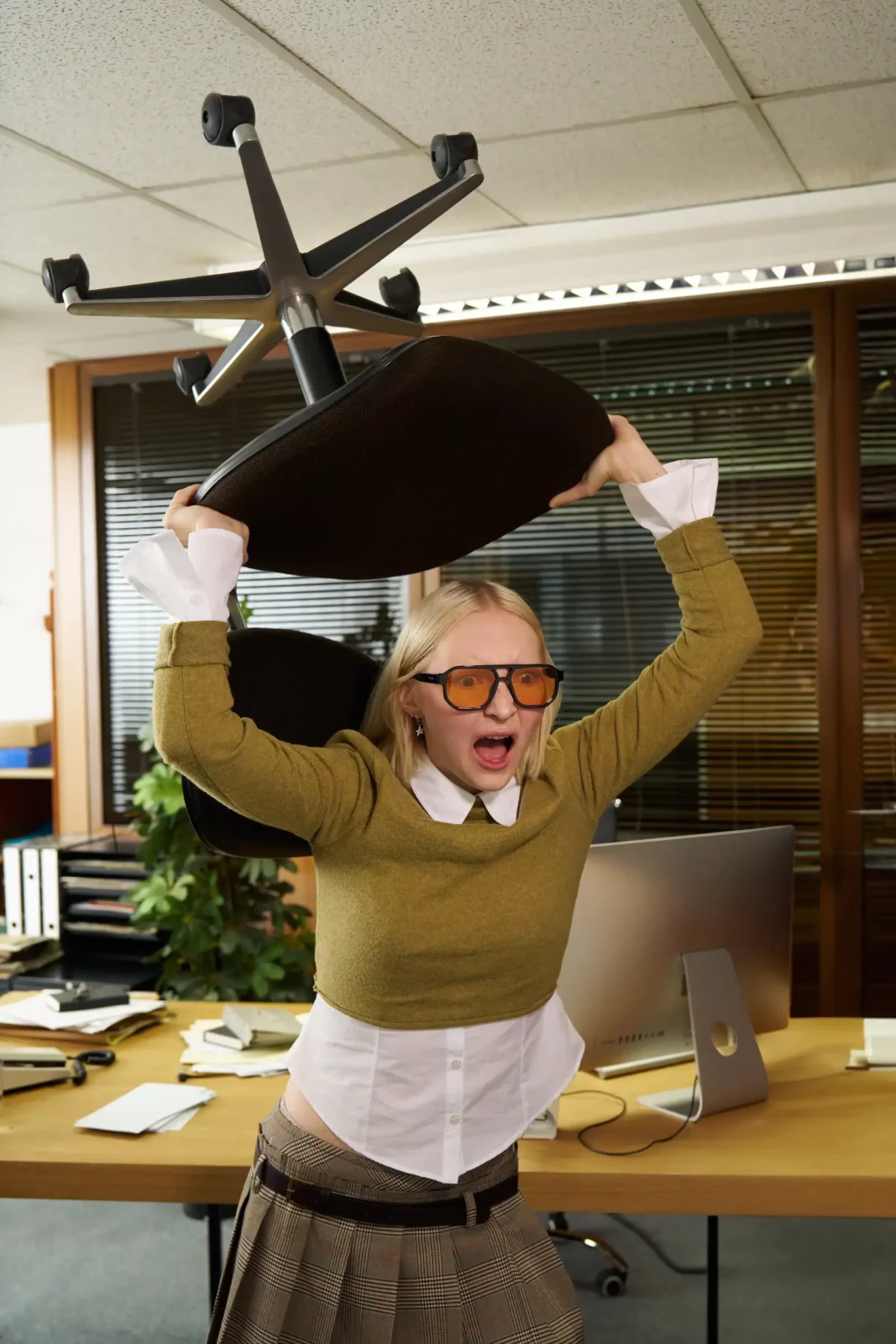 Man in sunglasses and a green sweater raising a large office object over his head.