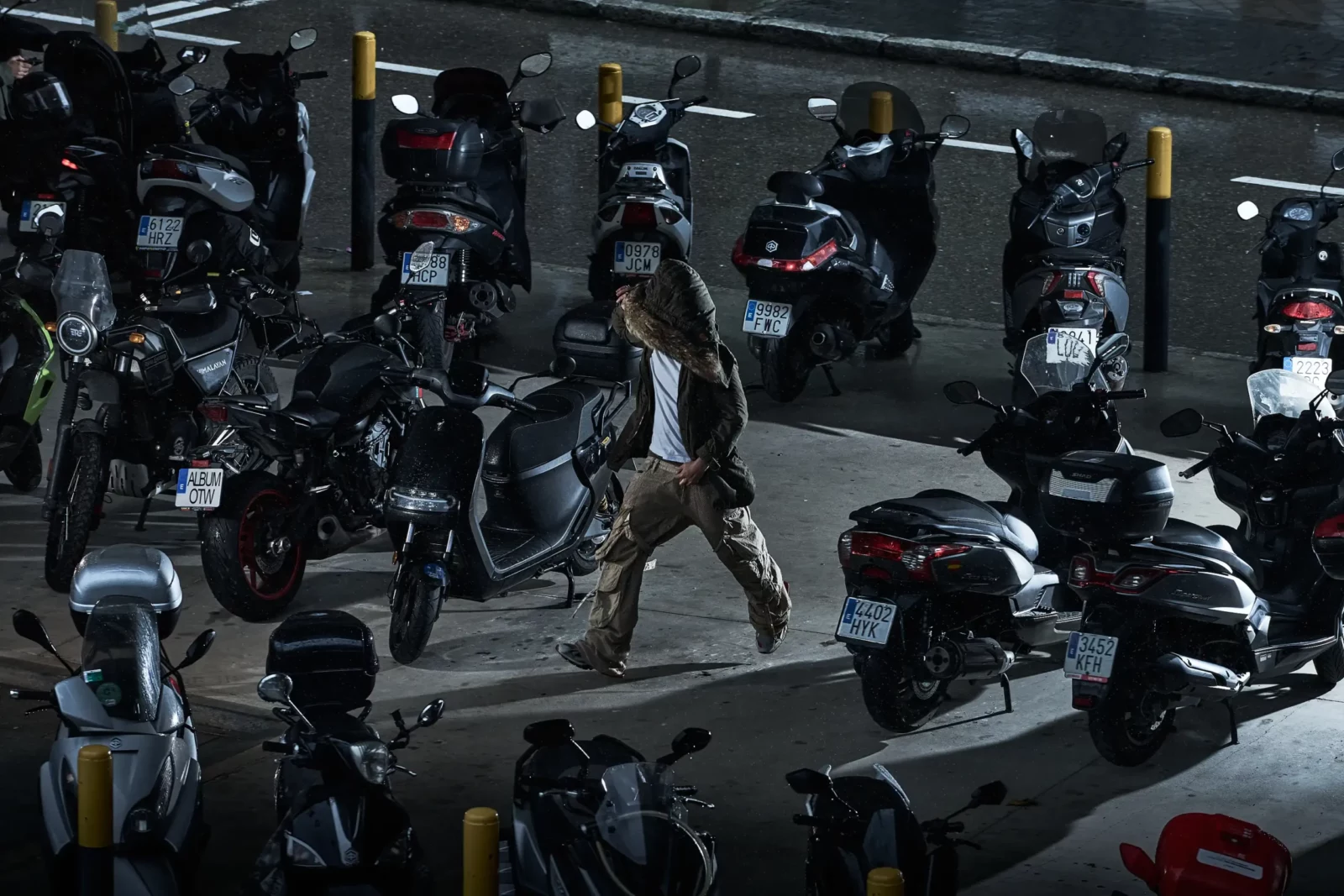 Overhead urban photograph of a model in a fur-trimmed hood walking among parked motorcycles.