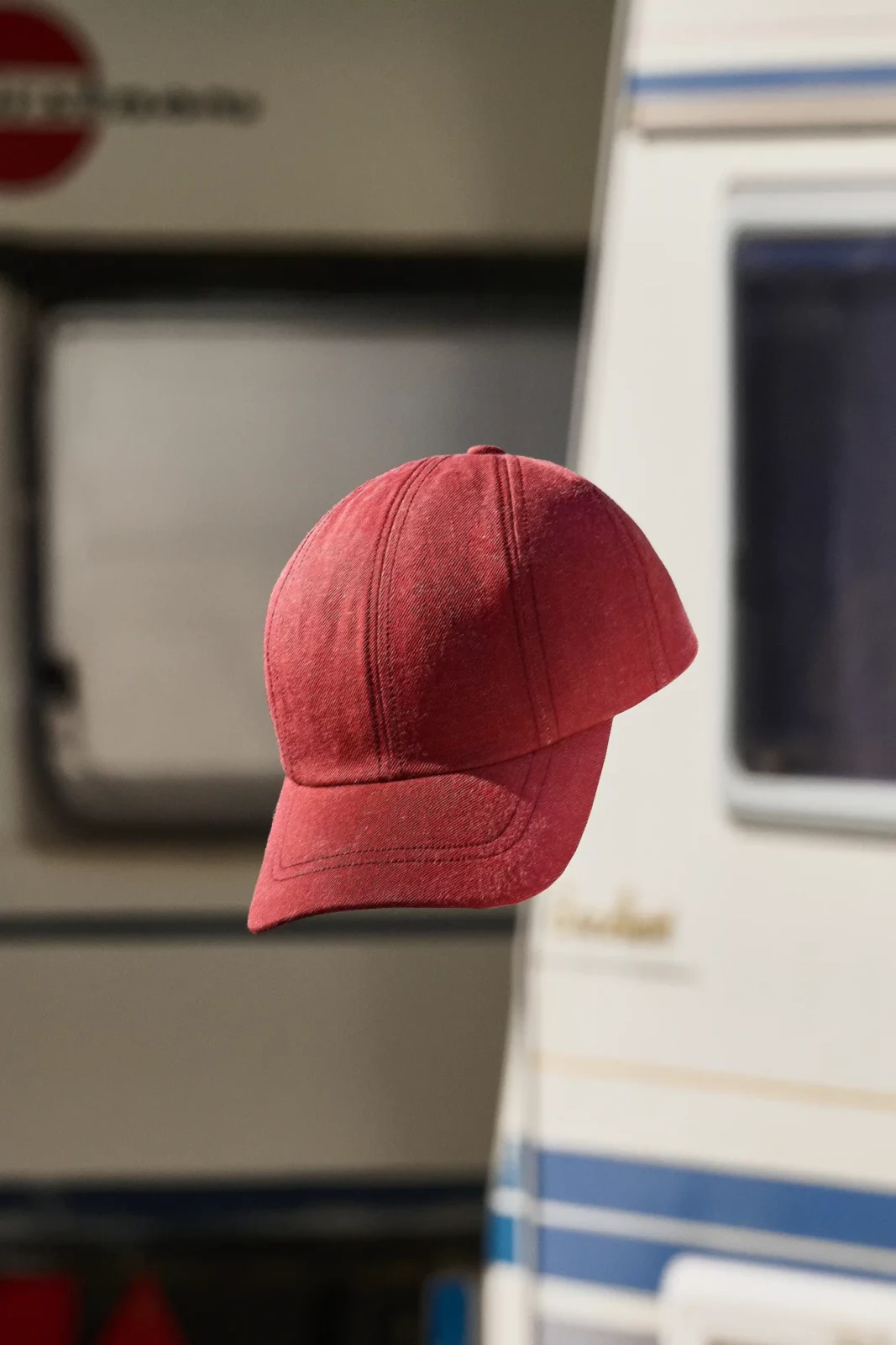 Close-up of a red baseball cap floating against a softly focused caravan background.