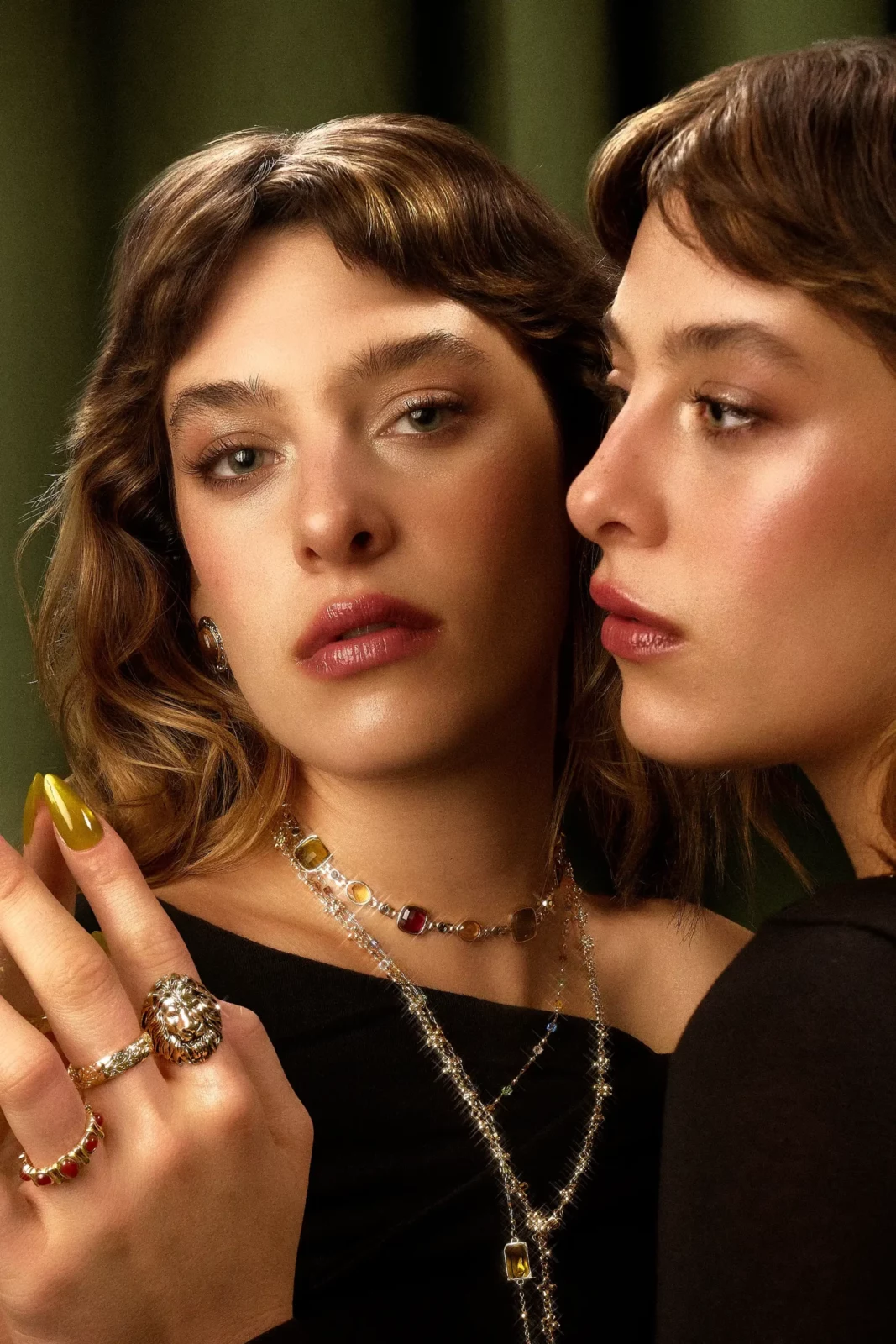 Two fashion models posing closely together in black outfits with silver necklaces and rings.