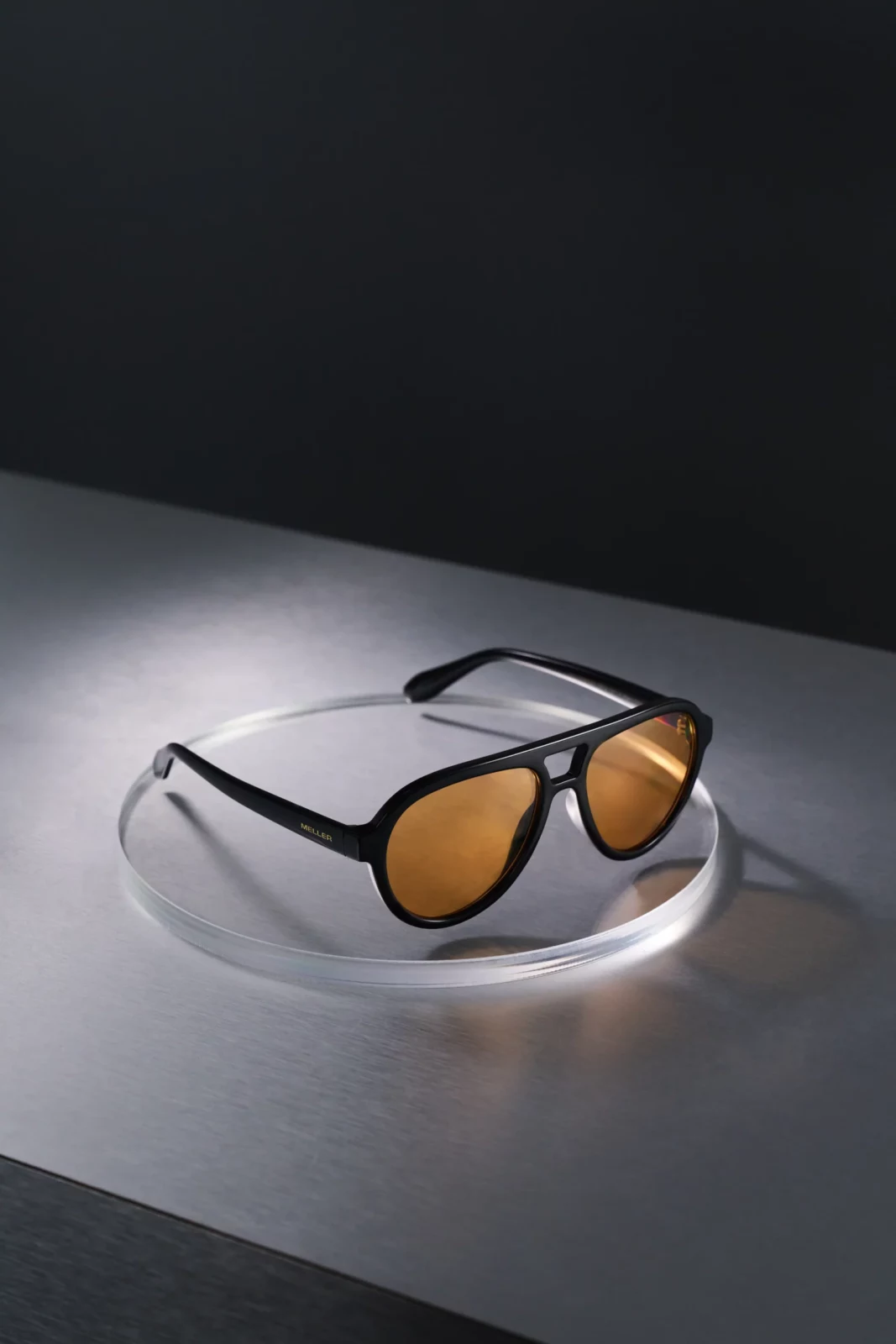 Still-life photograph of amber-lens sunglasses resting on a charcoal gray surface.