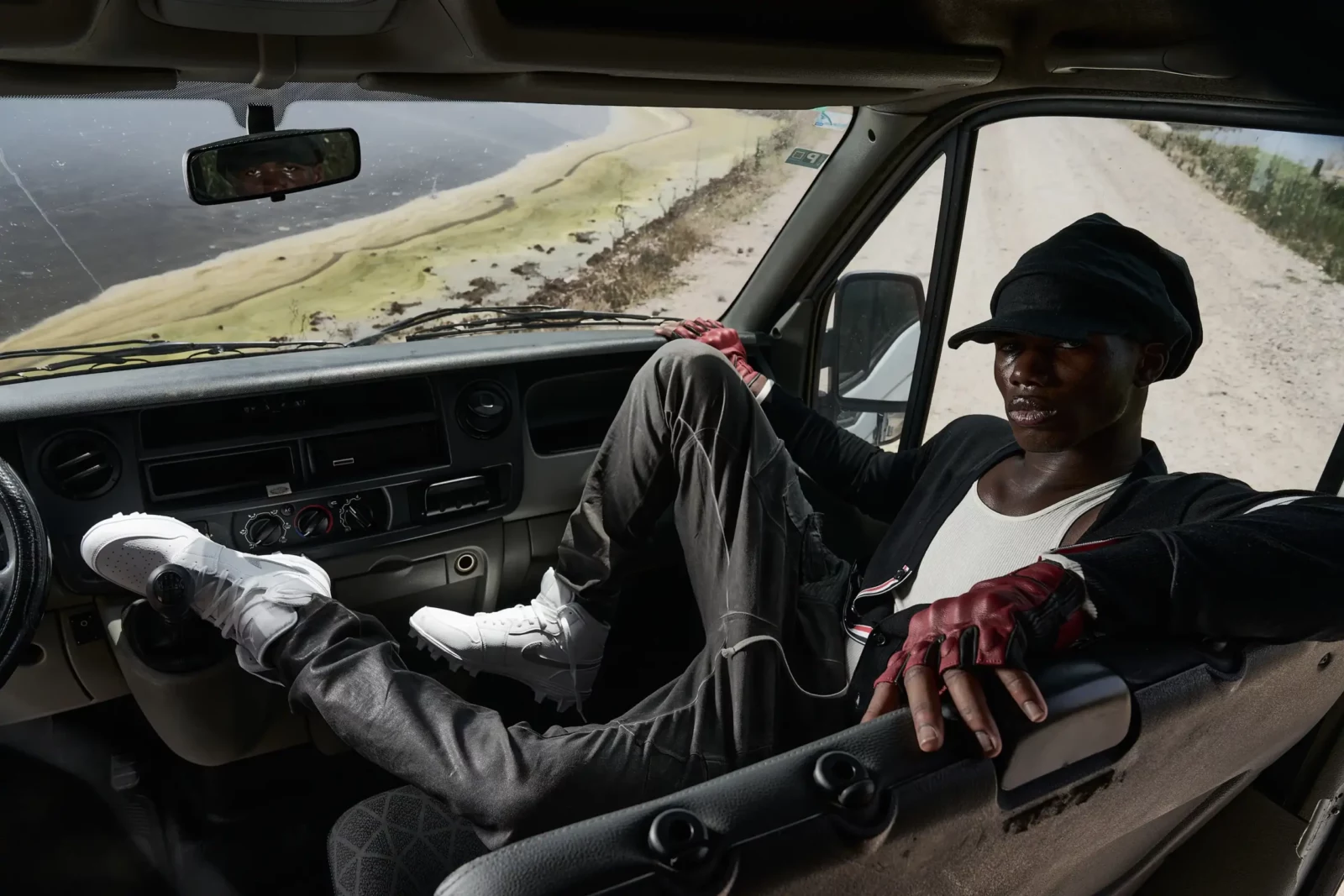Model reclining inside the cab of a truck wearing layered dark streetwear.