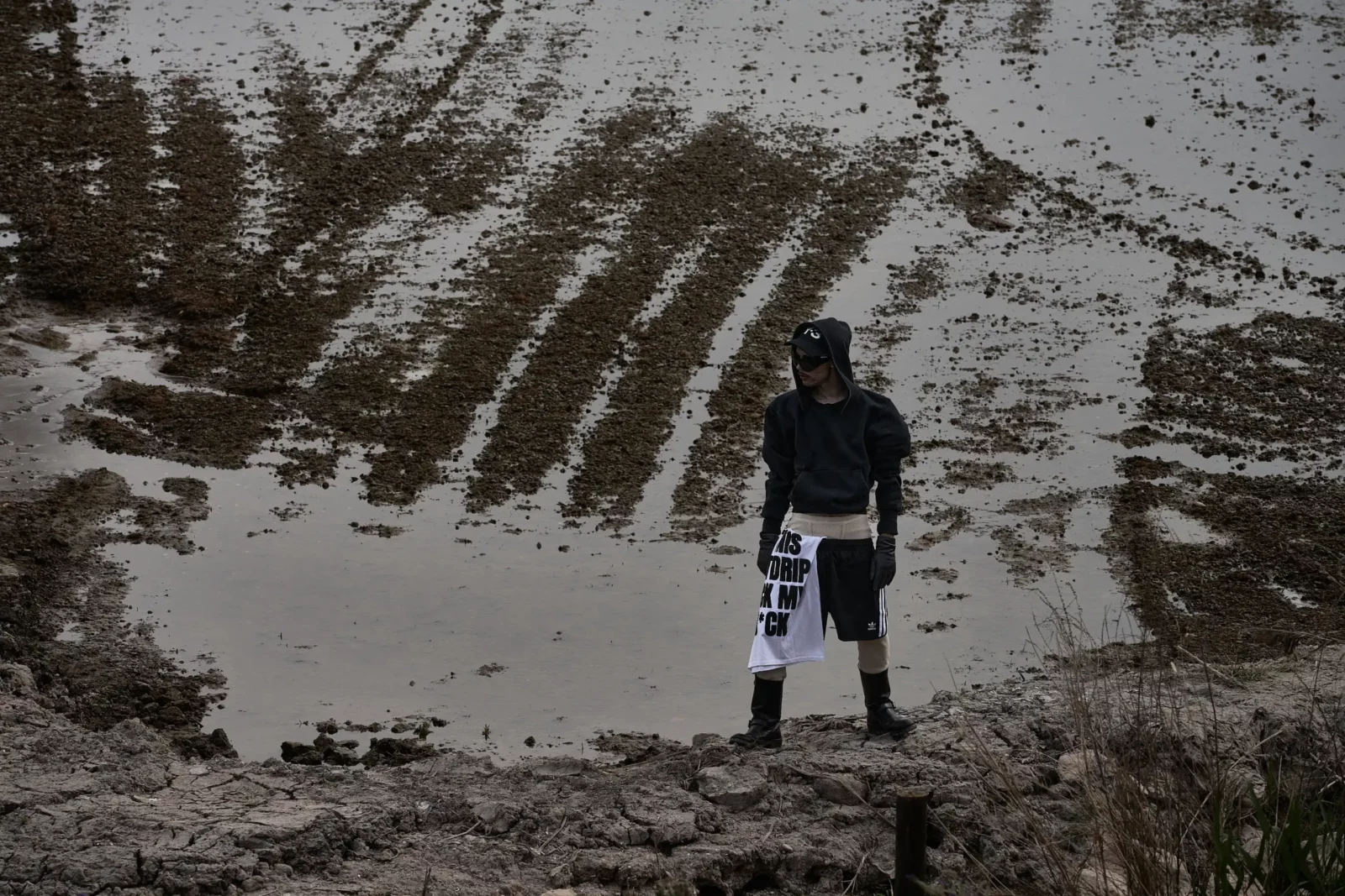 Distant figure in dark streetwear standing beside a flooded field.