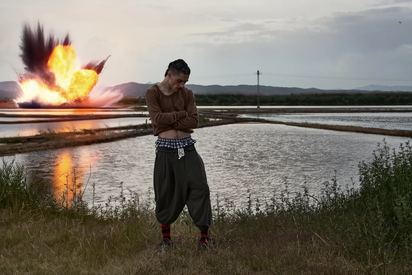 Model standing in front of an explosion-like burst of orange light near a wetland.