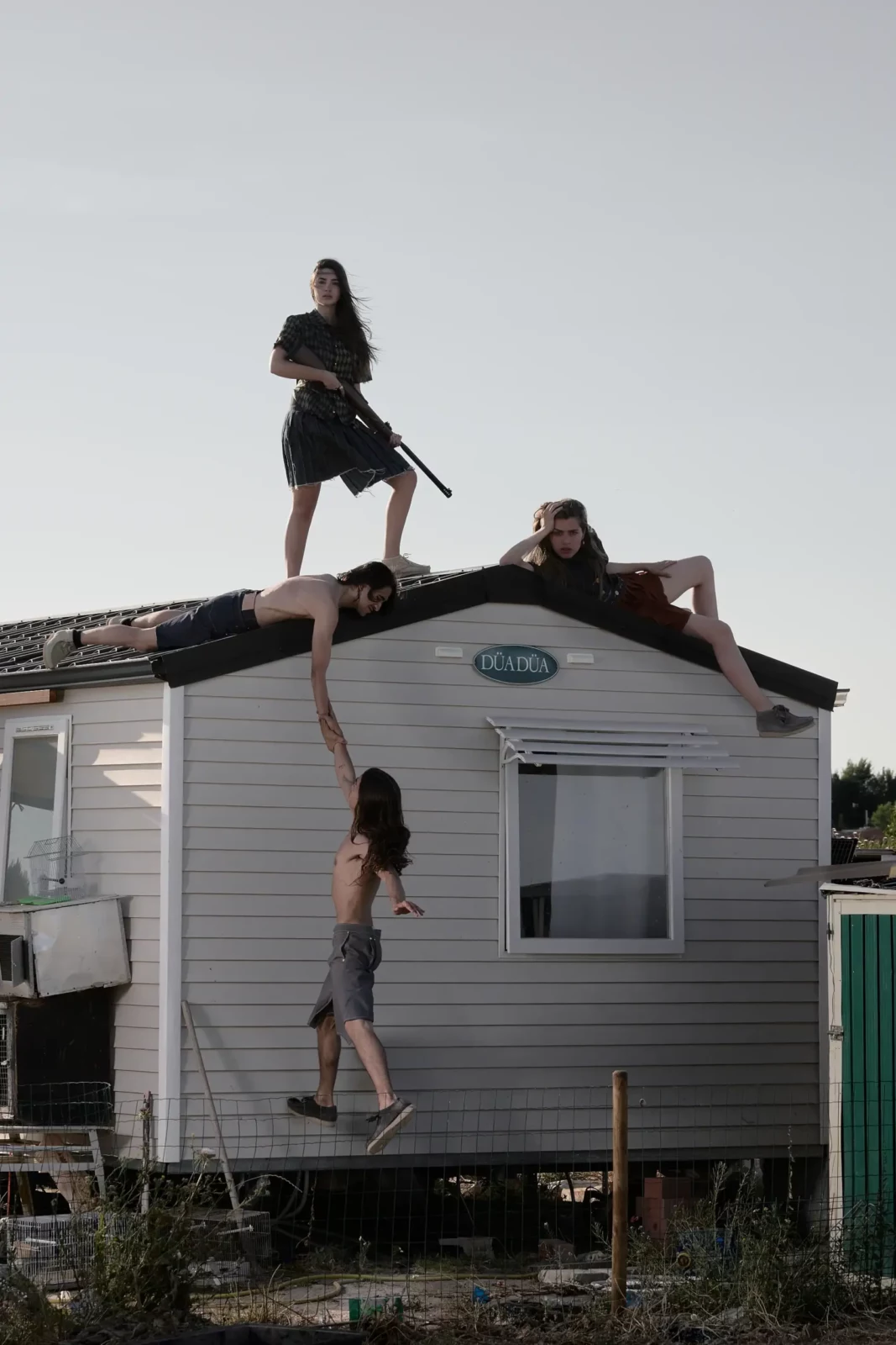 Two people climbing on and around a small caravan in a dry summer landscape.