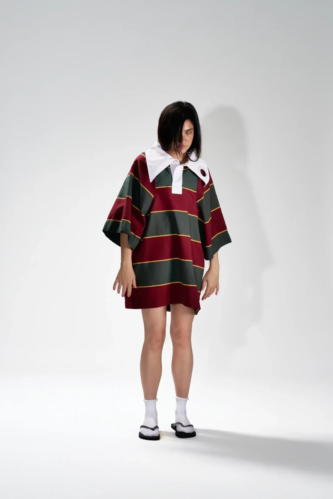 Full-length studio portrait of a model in a red and green striped oversized polo with white socks.
