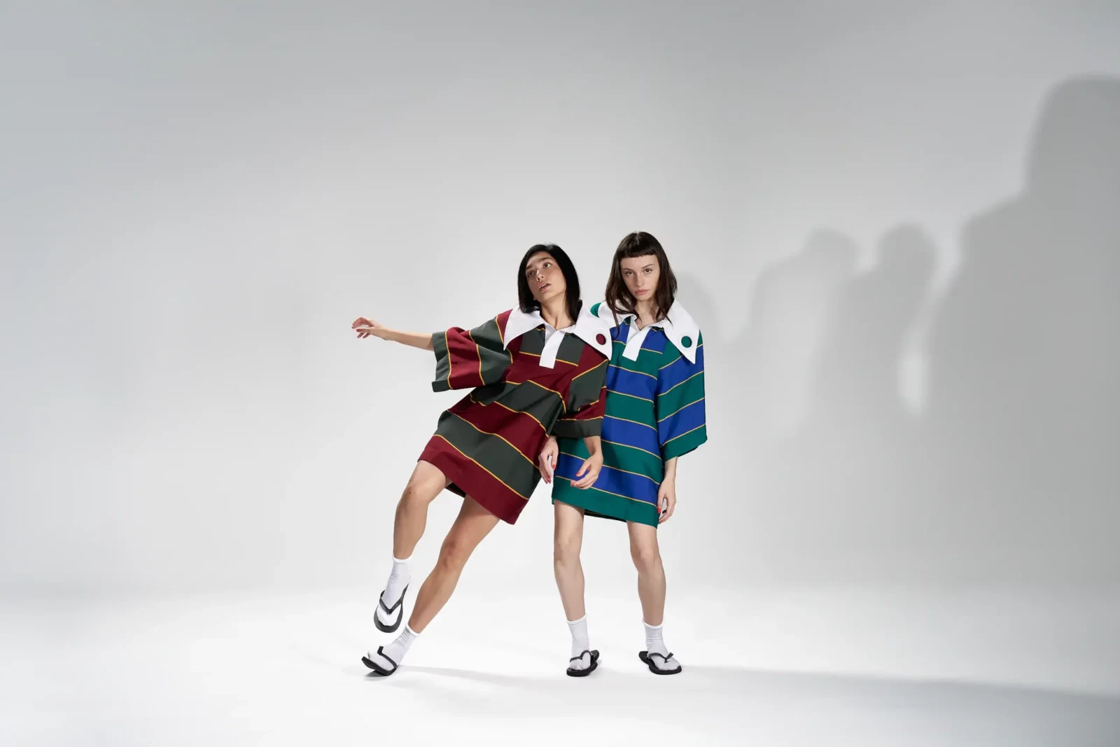 Two models in colorful striped polo shirts posing together against a minimal white studio background.