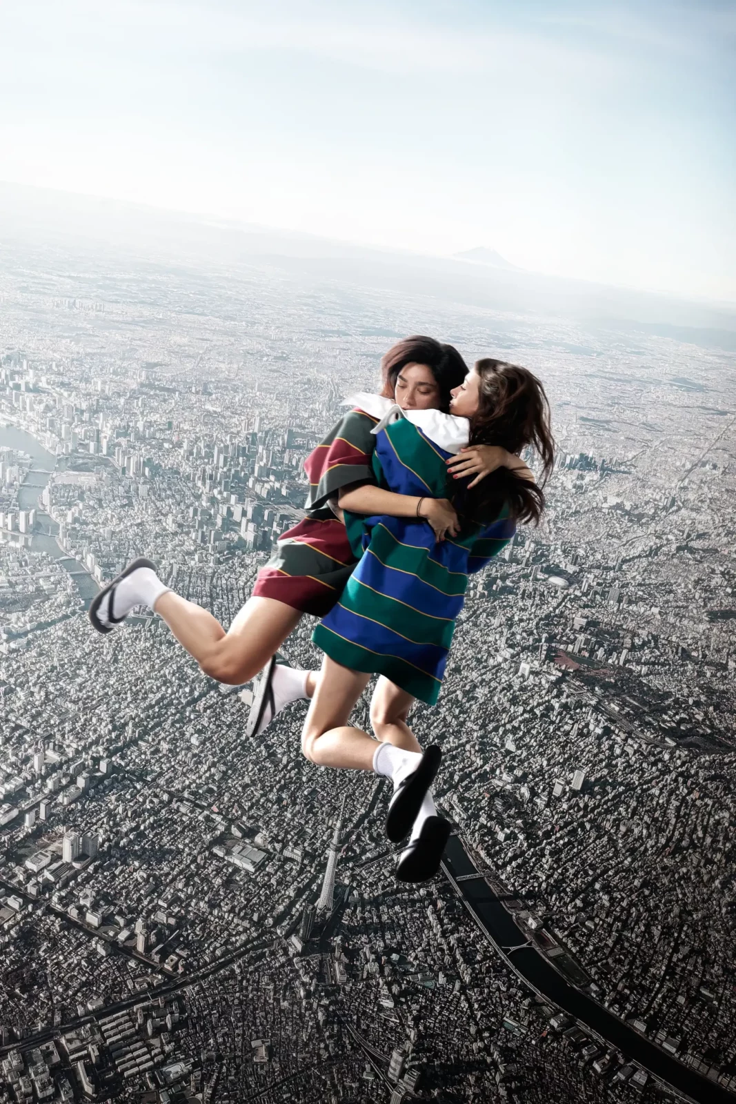 Two fashion models embracing on rocky ground in matching striped knit tops, photographed from above.