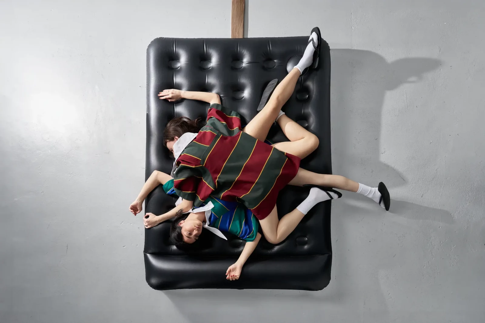 Overhead fashion photograph of two models wearing striped knitwear while lying across a black leather sofa.