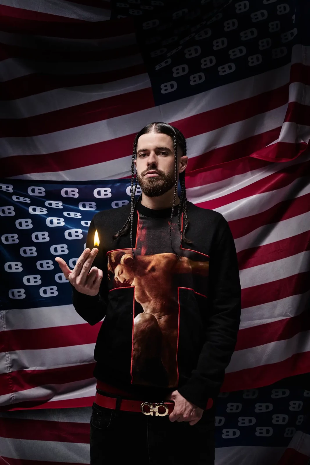 Portrait of a bearded musician wearing a printed black top in front of a large American flag.