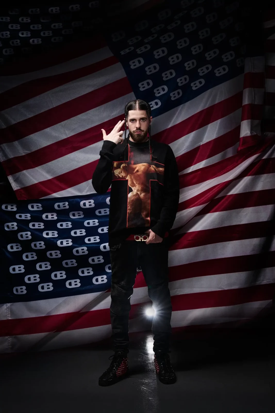 Full-length portrait of a musician standing in dark clothing in front of an American flag.
