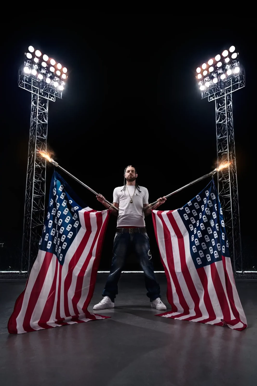 Wide night-time scene with a musician standing between illuminated American flags and stadium lights.