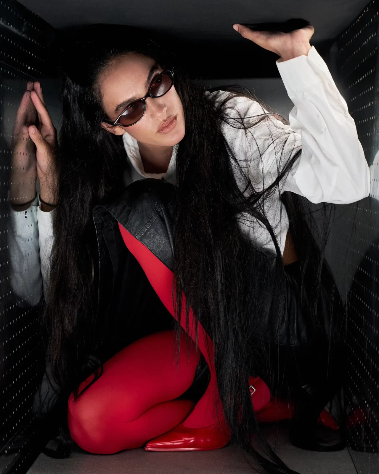 Fashion portrait of a model in black sunglasses and red-and-black clothing with hair swept across the face.