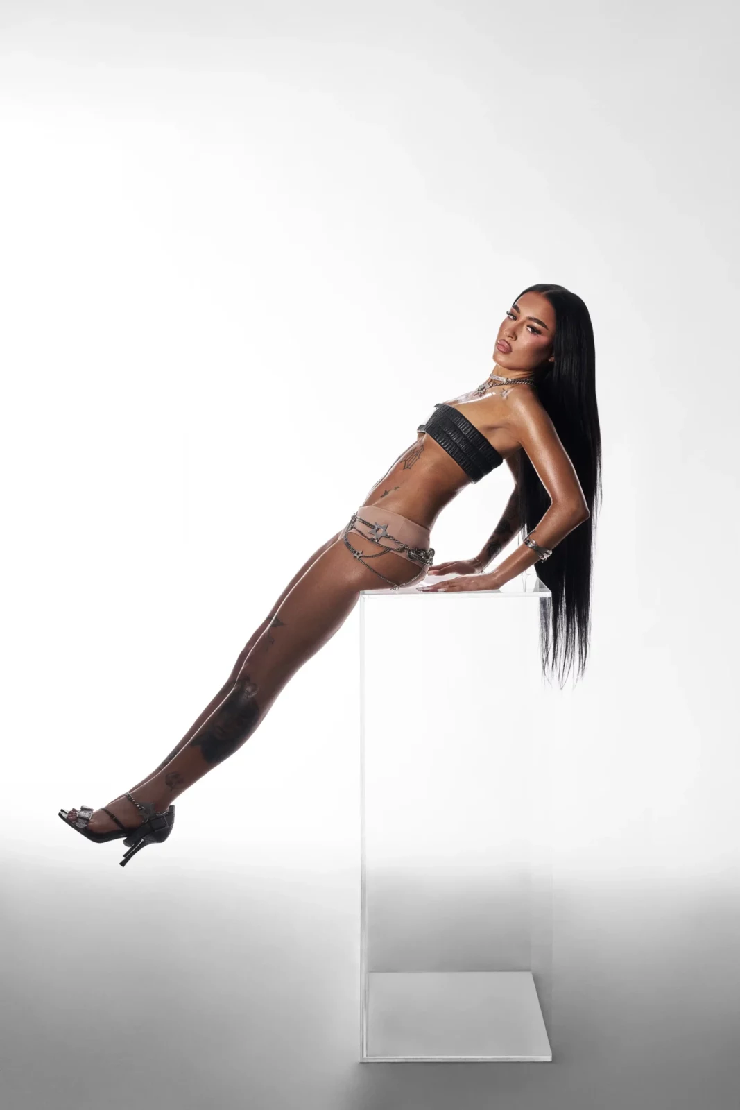 Woman reclining in heels with long black hair against a bright white studio backdrop.